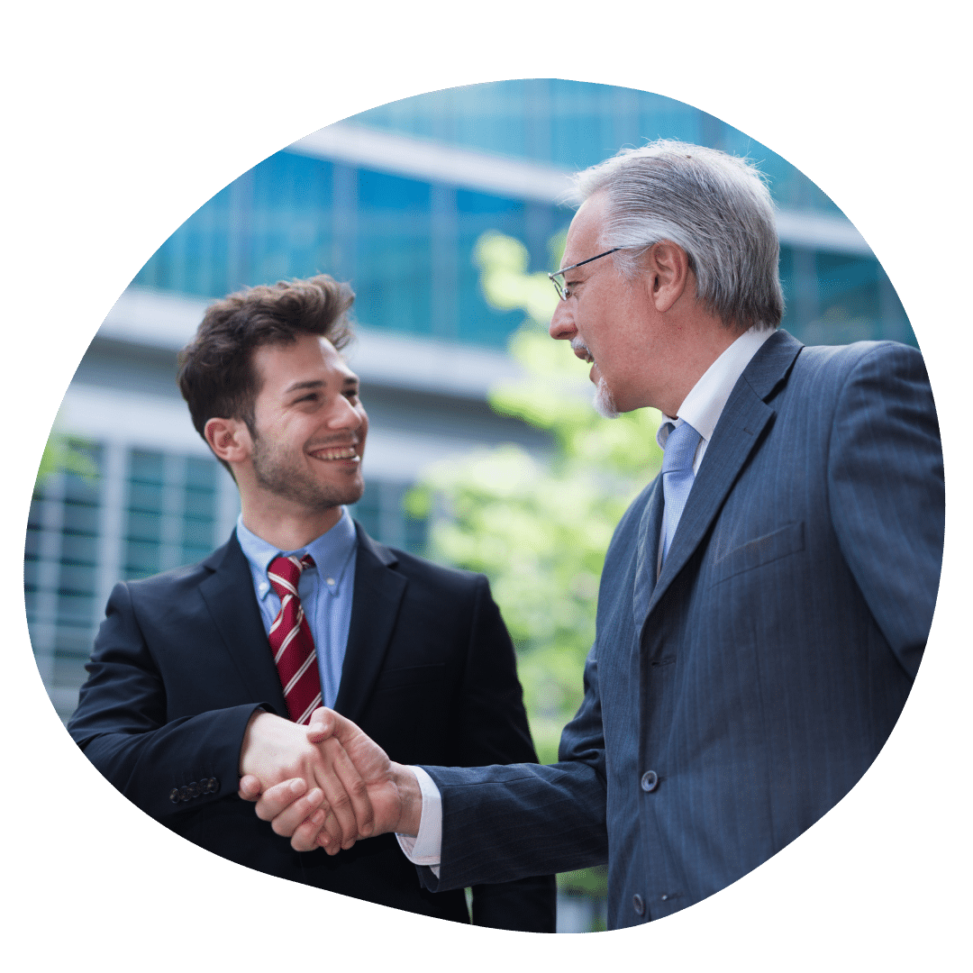 An MPP student dressed in a suit smiling shaking the hand of an older man also dressed in a suit